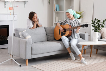 Teenage girl after chemotherapy playing guitar with her sister at home