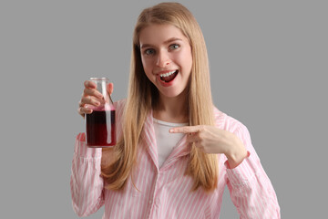 Young woman pointing at bottle of vegetable juice on grey background