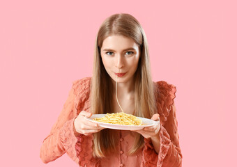 Young woman eating tasty pasta on pink background