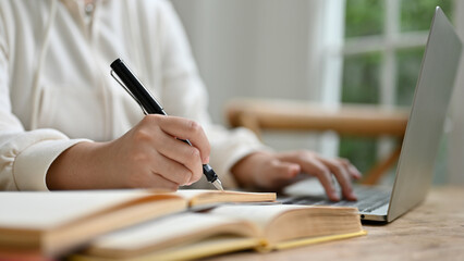 Close-up image of a female college student holding pen, writing or taking notes on a paper