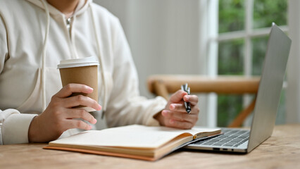 A young Asian woman sipping coffee and doing her homework in a coffee shop.