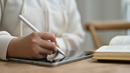 Close-up image of a woman holding a stylus pen, writing or taking notes on her digital tablet
