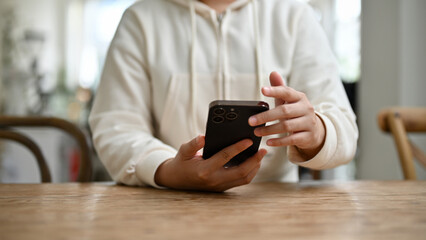 A woman chatting with her friends through her smartphone while sitting at a table in the cafe.