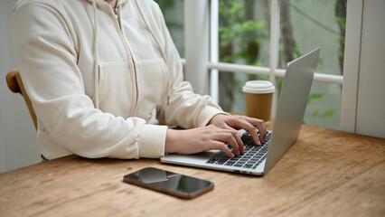 Close-up image of a female using her laptop at a table by the window in the coffee shop.