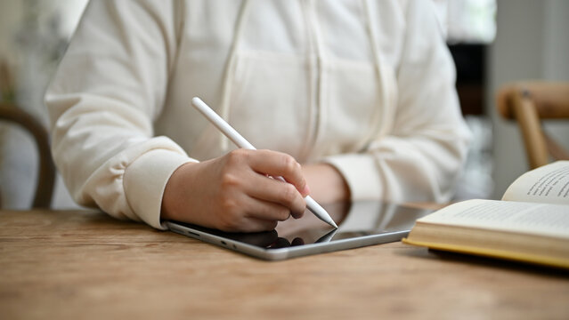 Close-up image of a woman holding a stylus pen, writing or taking notes on her digital tablet