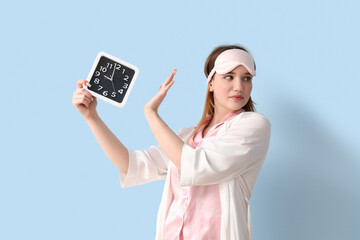 Young woman in pajamas rejecting clock on blue background