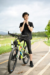 Fototapeta na wymiar A happy and handsome young Asian man in sportswear taking off his bike helmet after cycling