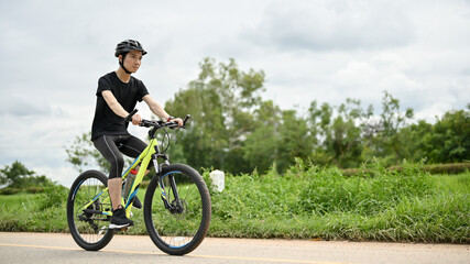 Fototapeta na wymiar A determined Asian man in sportswear and a bike helmet rides a bike along country roads.