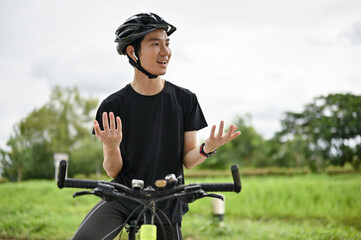 A handsome Asian man is talking with someone or dealing business on the phone while riding a bike
