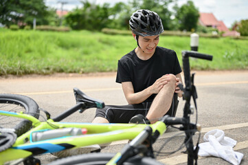 An injured young Asian male cyclist in sportswear and a bike helmet fell off the bike
