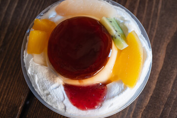 プラスチック容器の中のプリン。ホイップクリームと果物をトッピング。