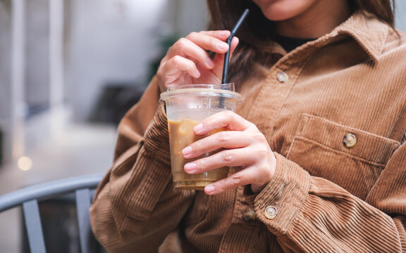 Closeup image of a woman holding and drinking iced coffee