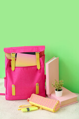 Pink school backpack with books, pencil case and houseplant on white wooden table near green wall