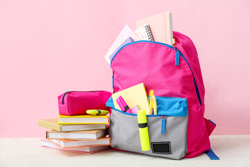 Pink school backpack with books, pencil case and markers on white table near color wall