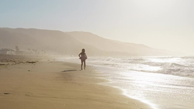 Happy little girl running by sandy beach at scenic sunset. Child dream concept in slow motion shot on RED camera. Adorable kid running along ocean shore in sunshine. Happy family concept. Child dream