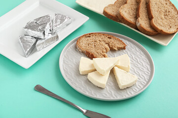 Plate with triangles of tasty processed cheese and bread pieces on turquoise background, closeup