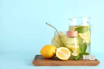 Sports bottle and jug of lemonade with cucumber on blue background