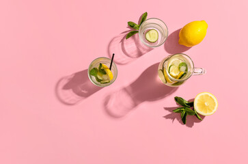 Glasses and jug of lemonade with cucumber on pink background