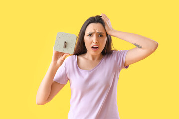 Stressed young woman with clock on yellow background. Deadline concept