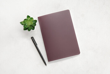 Brown notebook with pen and houseplant on white background