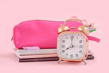 Alarm clock with notebooks and pencil case on pink background