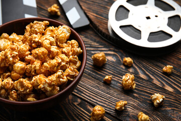 Obraz na płótnie Canvas Bowl with tasty popcorn, clapperboard and film reel on wooden background