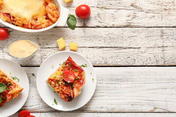 Plates and baking dish of pasta with tomato sauce on white wooden background