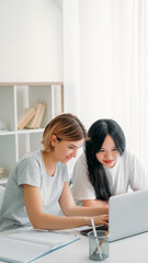 Studying teamwork. Learning cooperation. Homework together. Two happy young girls typing on laptop browsing internet for school research project at home workplace.