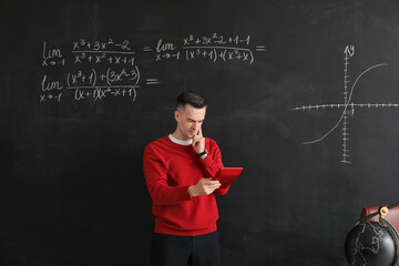 Thoughtful Math teacher with calculator near blackboard in classroom