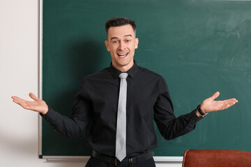 Happy male teacher near chalkboard in classroom