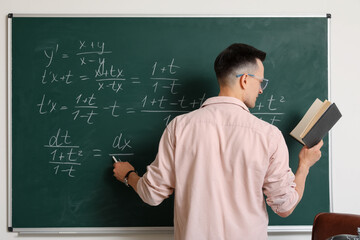 Male Math teacher conducting lesson near chalkboard in classroom, back view