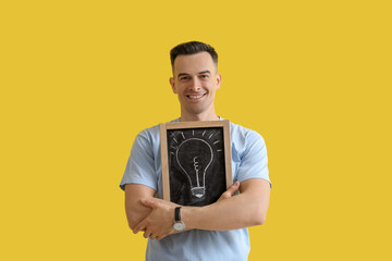 Male teacher holding chalkboard with drawn light bulb on yellow background