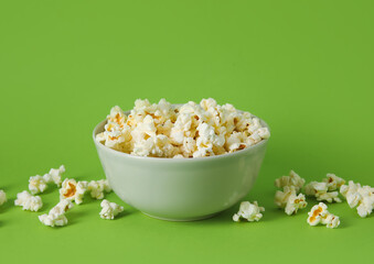 Bowl with tasty popcorn on green background