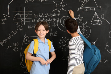 Little boys with backpacks near blackboard