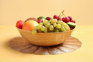 Bowl with different fresh fruits on orange background