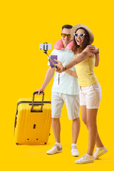 Young couple with passports and suitcase taking selfie on yellow background