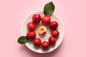 Plate with sweet cherries and leaves on pink background
