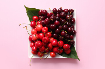 Plate with sweet cherries on pink background