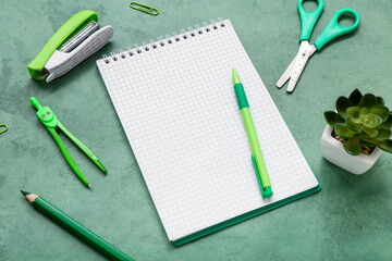 Blank notebook with stationery and houseplant on grunge green background