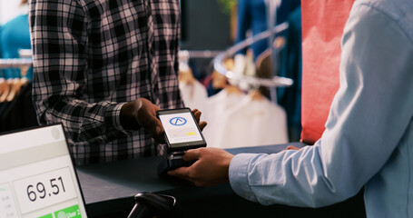 African american man paying for casual wear using mobile phone nfc on pos terminal, buying stylish...
