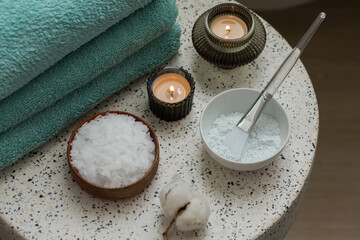 Composition with cosmetic alginate facial mask for spa treatments, aroma oil, epsom or magnium salt, candles and terry towels on a terazzo table