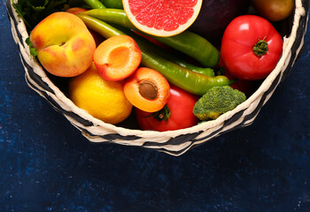 Wicker bowl with different fresh fruits and vegetables on blue background, closeup