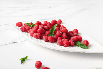 Plate with fresh raspberries and mint on white background