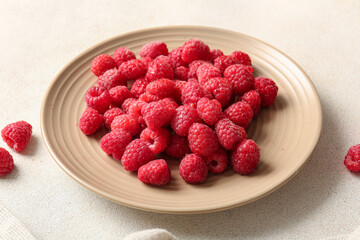Plate with fresh raspberries on white background