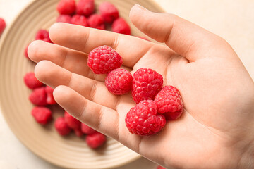 Female hand holding fresh raspberries and plate with berries, closeup