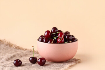 Bowl with sweet cherries on orange background