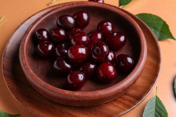 Bowl with sweet cherries and leaves on orange background