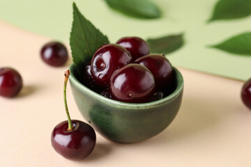 Bowl with sweet cherries and leaves on colorful background