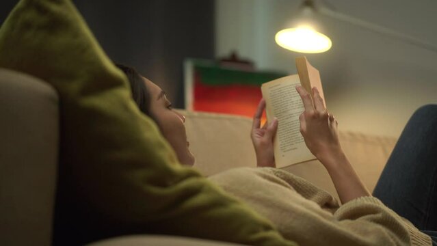 Close-up Happy woman opening, reading and relaxing a book on relax time at home. Vacation time of female reading a book on sofa at night. Education concept.