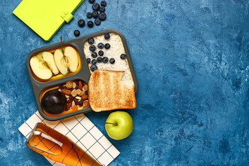 Bottle of lemonade, notebooks and lunchbox with tasty food on grunge dark blue background